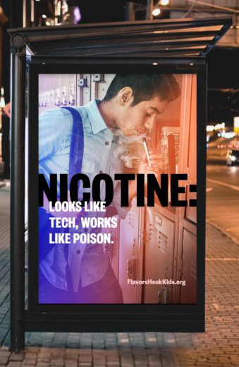 Bus stop billboard ad. Featuring male presenting teen leans into his locker at school and takes a drag of a vape pen. There is text over the image in black and white that reads “Nicotine: looks like tech, works like poison. “Flavorshookkids.org” is in the bottom right side of the image.
