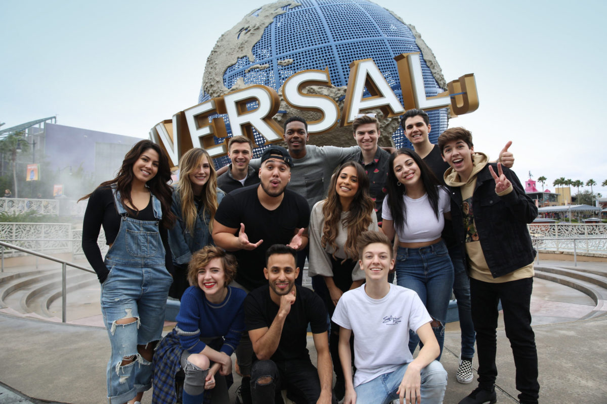 A diverse group of young adults pose and smile in front of the universal studios lifesize logo in Orlando, Florida.
