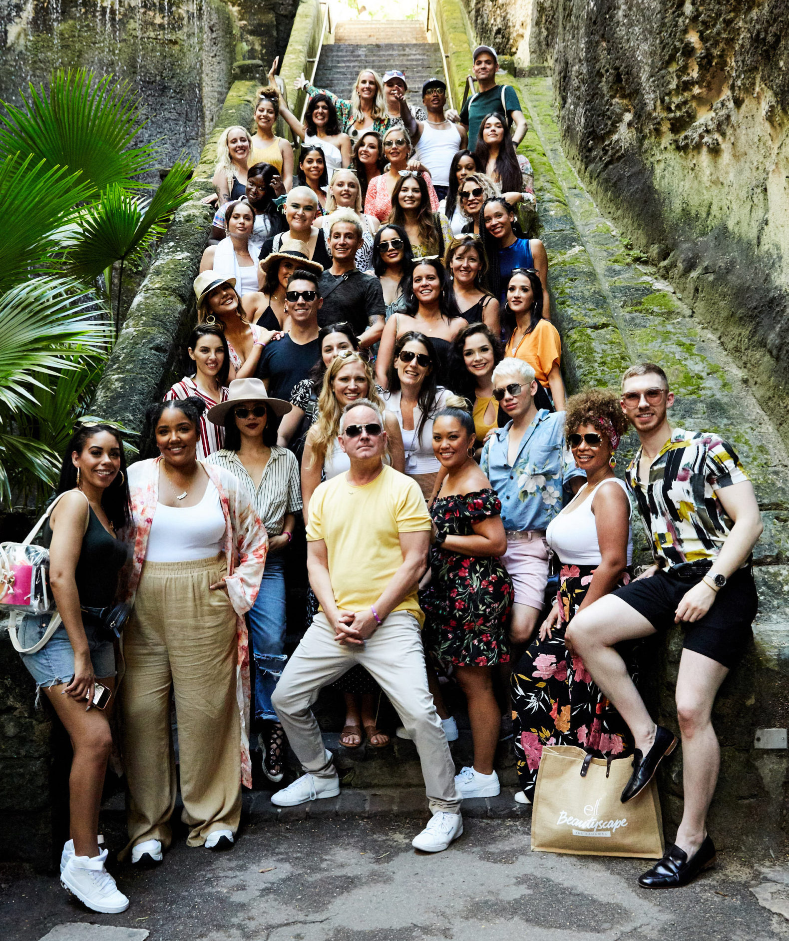 Large group shot of Beautyscape influencers standing on  beautiful old stairway in the Bahamas. Everyone is smiling.