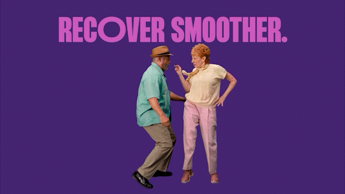 GIF on dark purple background showing a man in khakis, teal blue bowler shirt and tan panama hat dancing and doing a hip bump with a woman wearing light pink slacks and light yellow t-shirt with orange neck scarf. Copy above them in large, bold pink type reads, “Recover Smoother.” then flashes to thin white type reading, “Now there’s medication to treat COVID-19.”