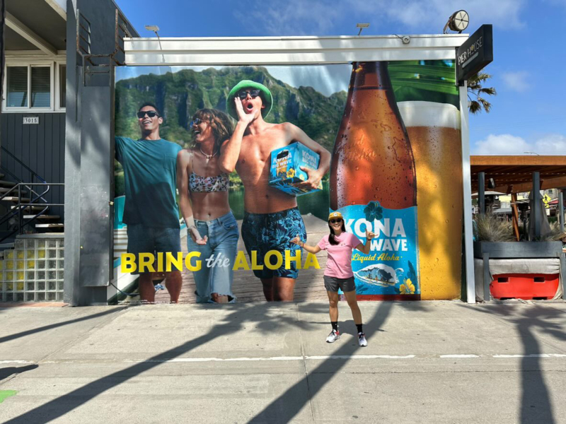 A billboard showing three friends on a dock in Hawaii. One of them is holding a case of Kona Big Wave. It has big “let’s get this party started” energy. The brand tagline, “Bring the Aloha,” is over the image.