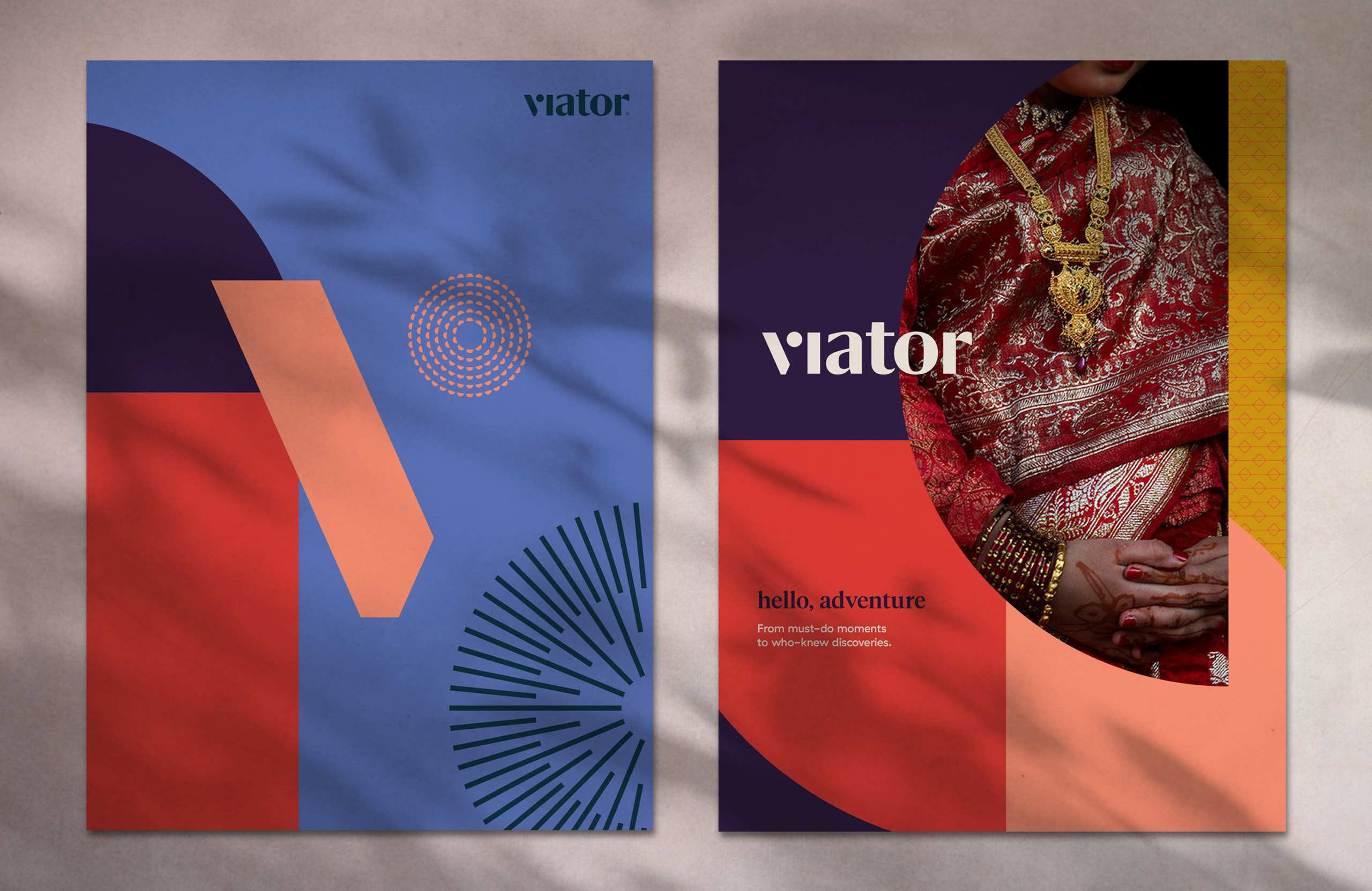 Colorful poster advertisements for Viator are displayed against a concrete wall. Featured images among the poster set: a person in a deep red sari, ornate gold necklace and stack of wrist bangles, paired with the brand’s new tagline “Hello, adventure.” Also included: boats on a gloomy lake in Phuket, and rolling golden hills of Tuscany.